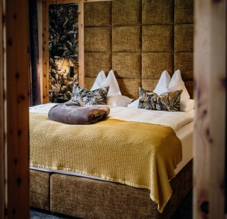 Rieser - Zimmer Betthaupt/Wandbespannung hinter Bett in gelben Stoff abgesteppt, Wandbespannung seitlich gelb gemustert Junglestoff, Zierkissen in gelben Junglestoff, Tagesdecke in grau, Bettüberwurf in gelb